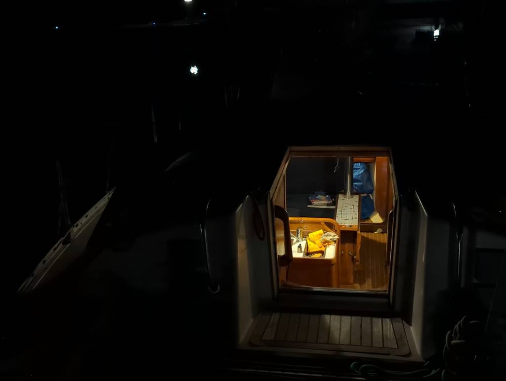 The interior of our boat at night: wooden furniture, a sink, sailing books.