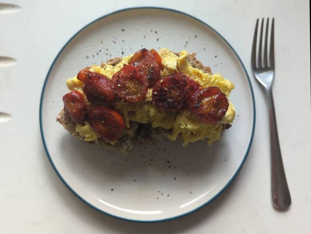 The aforementioned scrambled eggs on a plate, with the tomatoes placed on top and lots of salt and pepper.